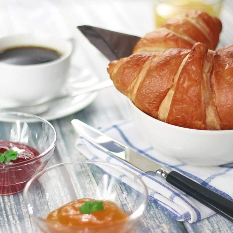An almond croissant in a white bowl, with coffee and preserves alongside