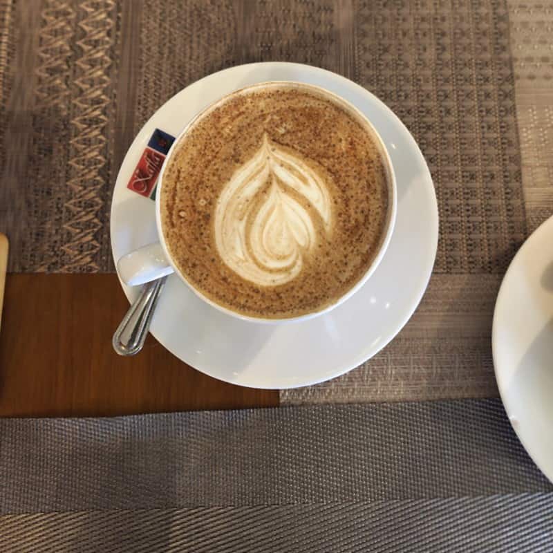 A cortado with a poured leaf pattern, seen from above on a white saucer