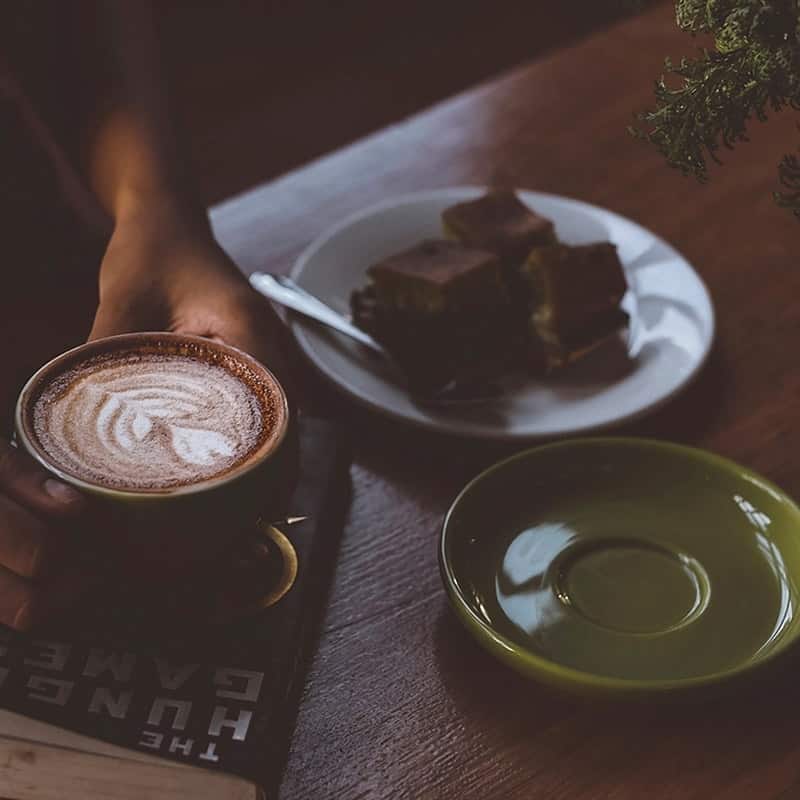 A brownie and a small milk coffee on a dark table