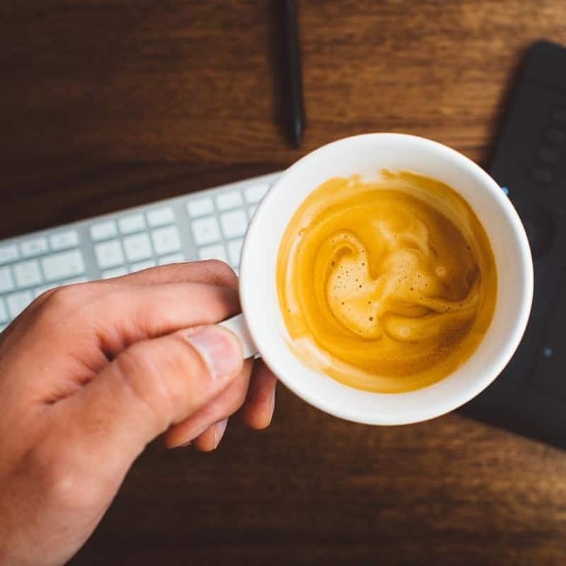 A short cup of espresso with a golden crema, held in one hand
