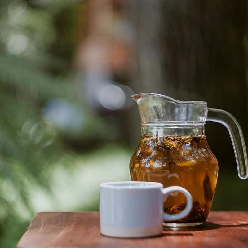 A glass pitcher of pale jasmine tea beside a small white cup