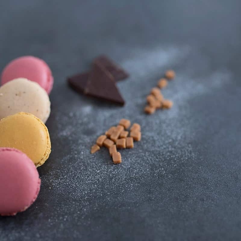 Macarons beside shards of dark chocolate on a slate surface