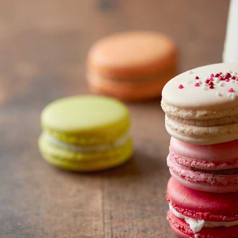 A pistachio macaron among pastel macarons on a wooden table