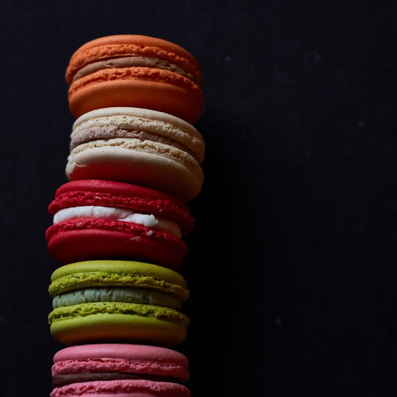 A tall stack of assorted macarons against a dark background