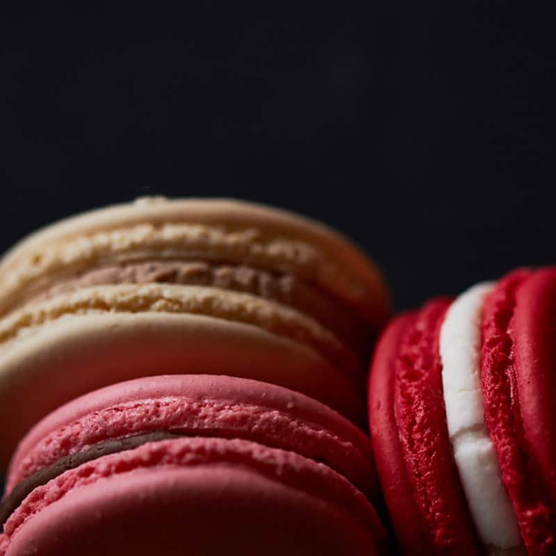 A cream vanilla macaron in a row of macarons against a dark background