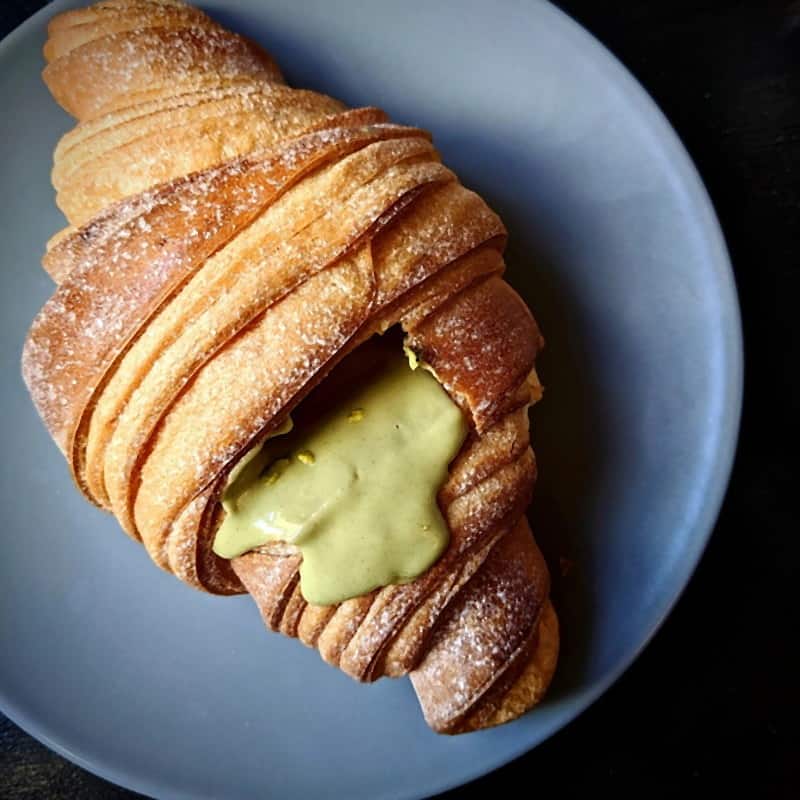 A sugar-dusted croissant filled with pistachio cream on a blue plate