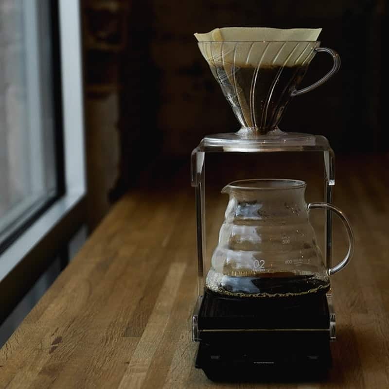 A glass pour-over cone and carafe on a brew scale, lit by a window