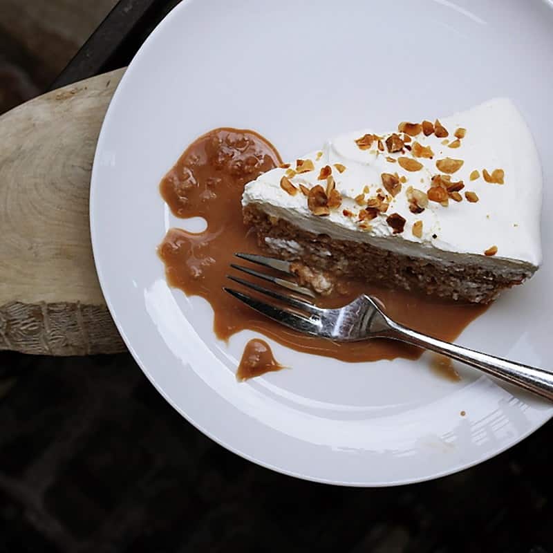 A slice of blondie with salted caramel and chopped nuts on a white plate