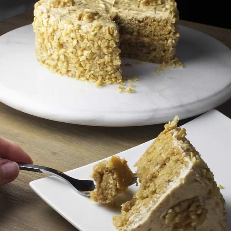 A walnut-crusted maple cake with one slice lifted onto a plate