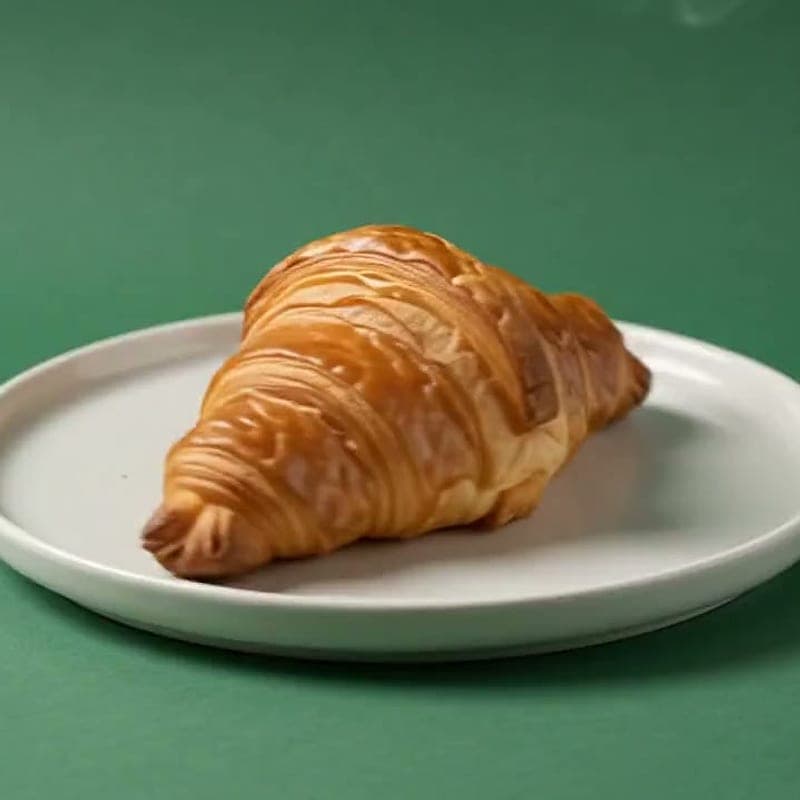 Golden butter croissant resting on a white ceramic plate