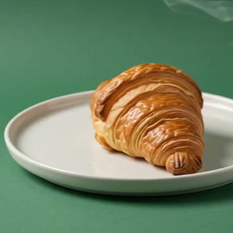 Pistachio croissant dusted with crushed pistachio on a ceramic plate