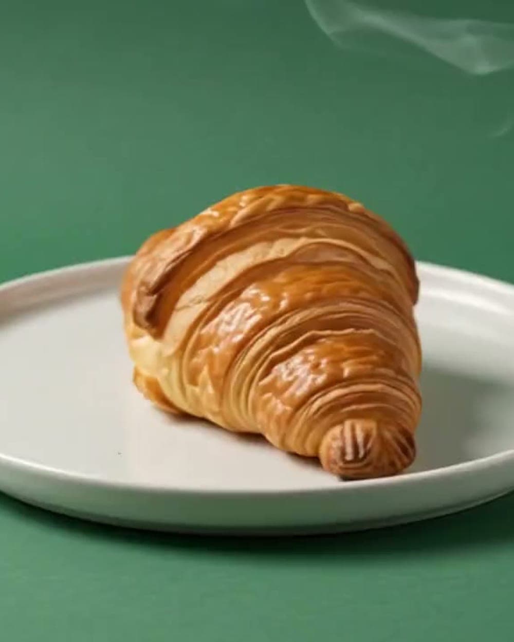 A finished butter croissant on a white ceramic plate, layers visible in the crust