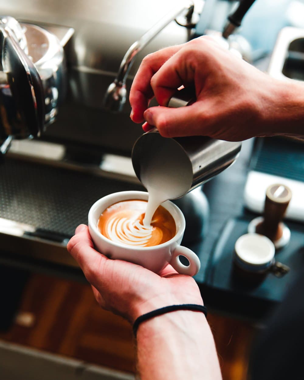 A barista pouring milk into a cup to finish a rosetta